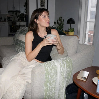 Frau sitzt auf Sofa und hält Tasse mit beiden Händen