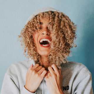 Biotina y Vitaminas para el Cabello: Mujer riendo, rizos llenos bajo la capucha