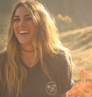 Una mujer sonriente en un campo, rodeada de elementos naturales.