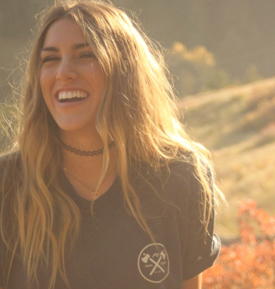 Una mujer sonriente en un campo, rodeada de elementos naturales.