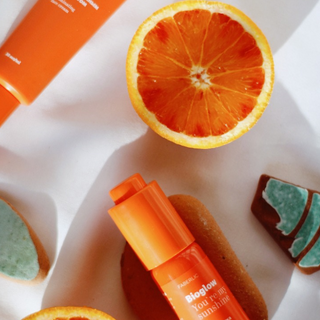 Elementos naturales como rodajas de naranja y una botella de suero de vitamina C están dispuestos sobre una mesa blanca.