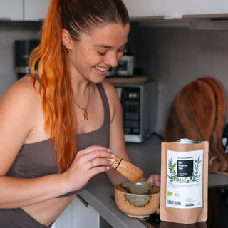 Una mujer preparando una taza de té en una cocina rodeada de elementos naturales.