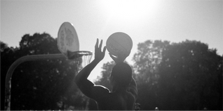 Un hombre atrapa un frisbee en una cancha de baloncesto, rodeado de elementos naturales.