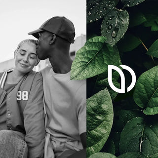 Una persona besa a otra en la sien con una sonrisa. Están sentados juntos, con un primer plano de hojas verdes con gotas de agua y una superposición de logotipo blanco visible cerca.